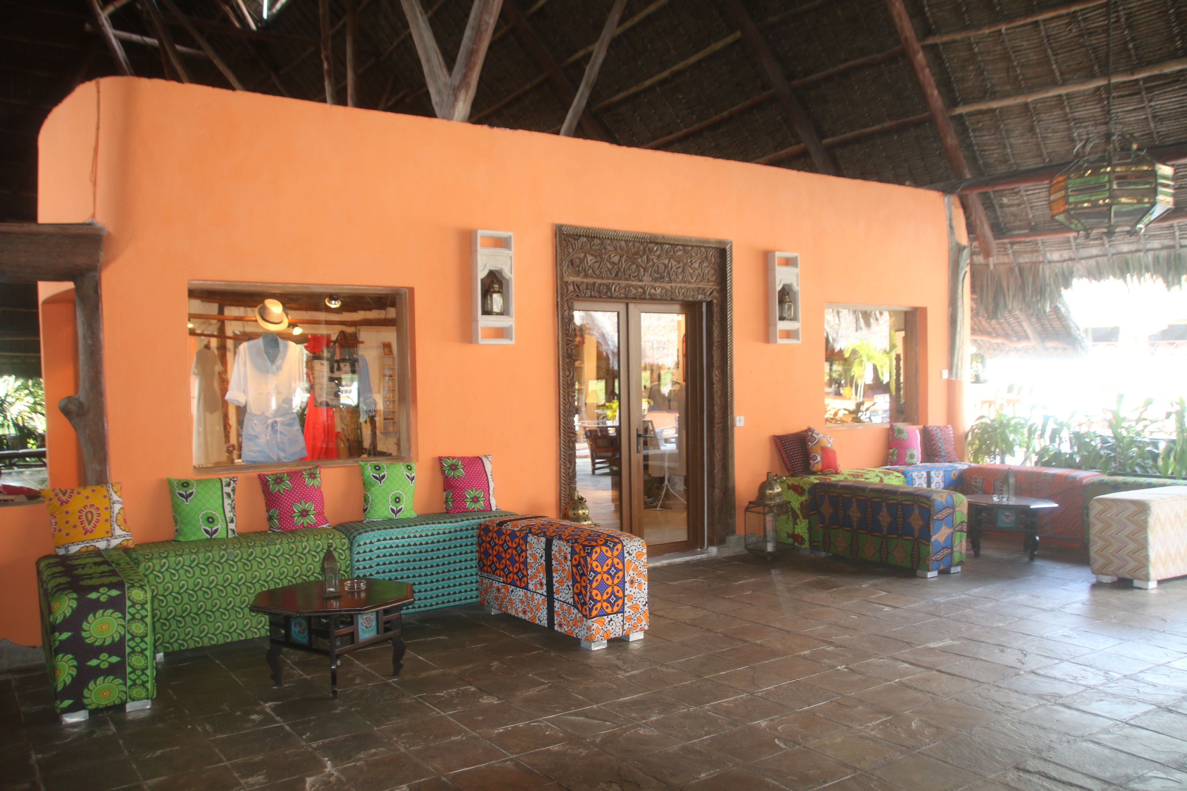 A spacious lobby with a high ceiling and a thatched roof. There are several colorful sofas and a small table in the center.