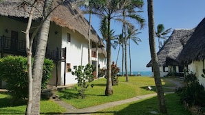 Un resort con cabañas de techo de paja, palmeras y una vista despejada del mar.