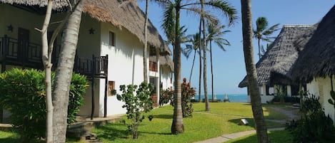 A resort with thatched-roof cottages, palm trees, and a clear view of the sea.