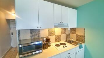 A compact kitchen with white cabinets, a microwave, a coffee maker, and a stove.