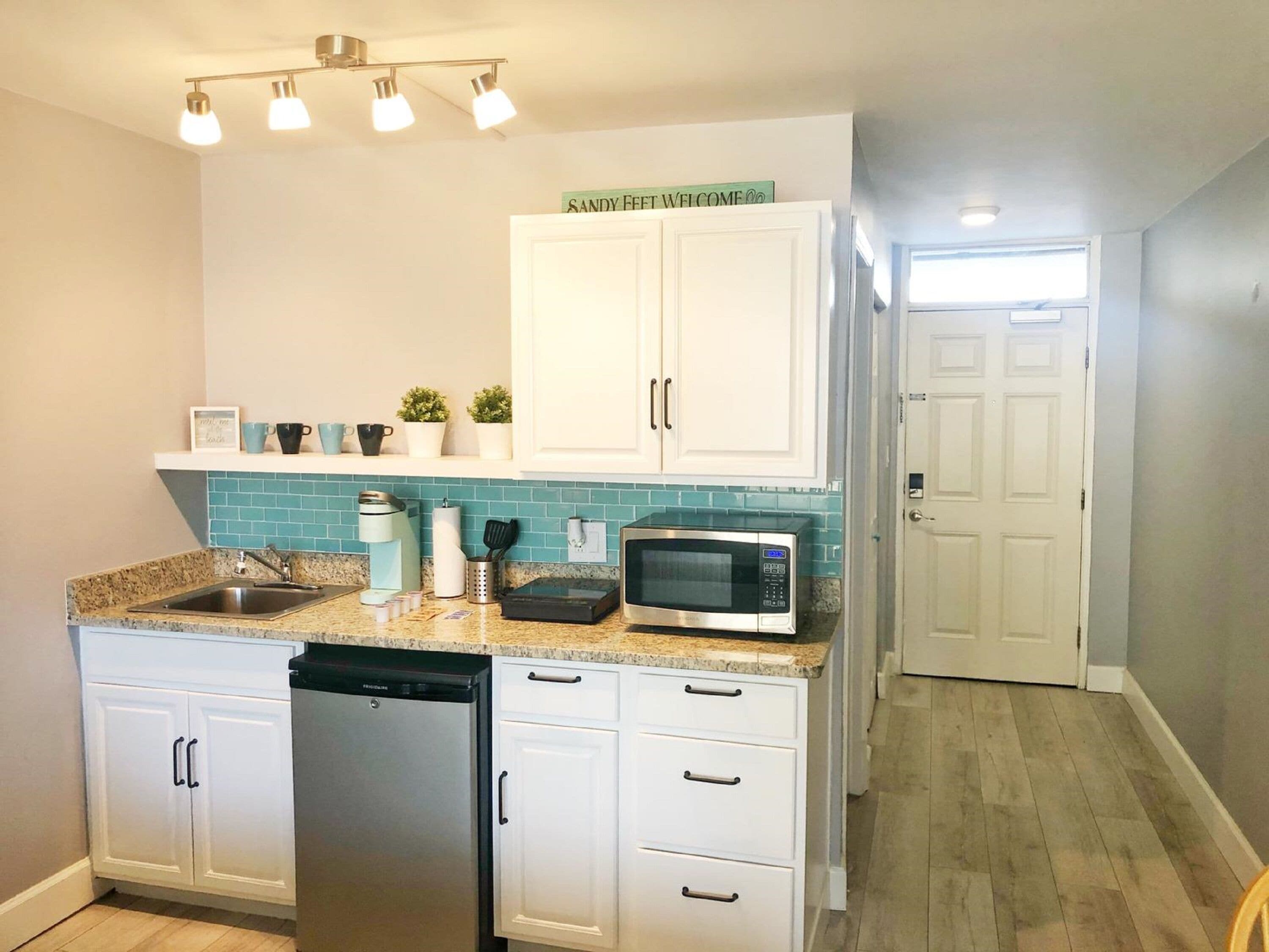 A compact kitchen with white cabinets, a built-in microwave, a dishwasher, and a countertop with a sink.