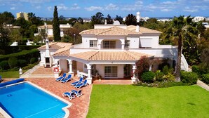 Ein großes, zweistöckiges Haus mit Swimmingpool, Liegestühlen und einem gepflegten Garten.