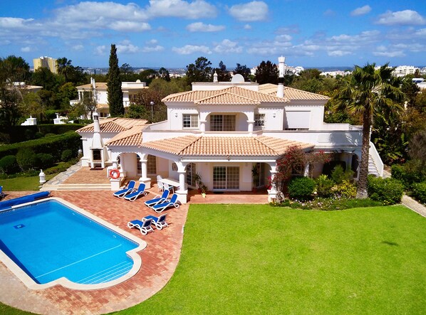 A large, two-story house with a swimming pool, sun loungers, and a well-maintained garden.