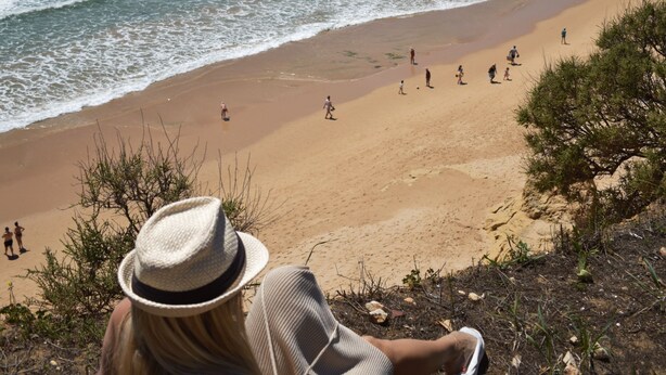 Ein Strand mit blauem Himmel, Felsformationen und Menschen, die Sand und Wasser genießen.