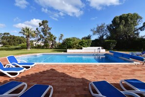 A pool area with blue lounge chairs and a clear blue sky.