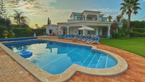 Ein Schwimmbecken mit Liegestühlen, eine überdachte Terrasse und ein großes Haus mit Garten.