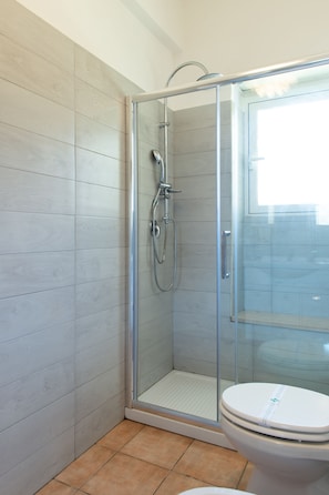 A bathroom with a glass-enclosed shower, a toilet, and tiled walls. - Pantarei (Rome)