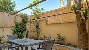 Um pátio externo com mesa e cadeiras, cercado por uma vedação de bambu e diversas plantas.