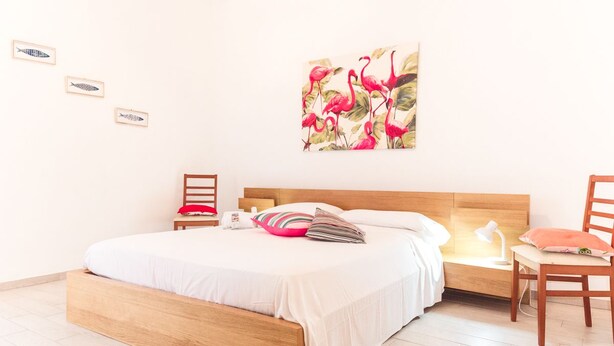 Een slaapkamer met een houten bed, een nachtkastje, een stoel en een wand met kunstwerken.