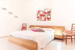Un dormitorio con cama de madera, mesita de noche, una silla y una pared decorada con cuadros.