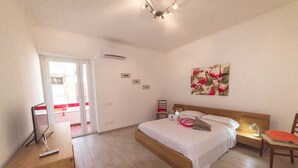 Een slaapkamer met een bed, nachtkastje, stoel en een schilderij aan de muur.