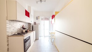 Een smalle keuken met witte kasten, een betegelde spatwand en een fornuis.