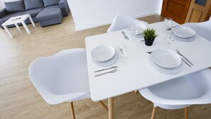 A modern dining area with a white table set for four, surrounded by white chairs, a grey sofa, and a small white side table. - SOBREMAR Apartment - STUNNING Views (Salou)