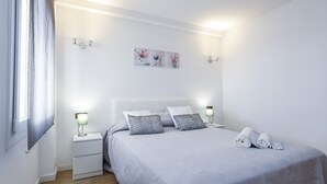A neatly made bed with a grey bedspread and two pillows, a bedside table with a lamp, and a wall-mounted artwork above the bed. - SOBREMAR Apartment - STUNNING Views (Salou)