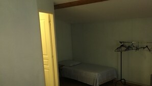 A bedroom with a bed, a bedside table, a chair, a wardrobe, and a hanging clothes rack. - Le Palmyre Soleil de l'Amazonie (La Douze)