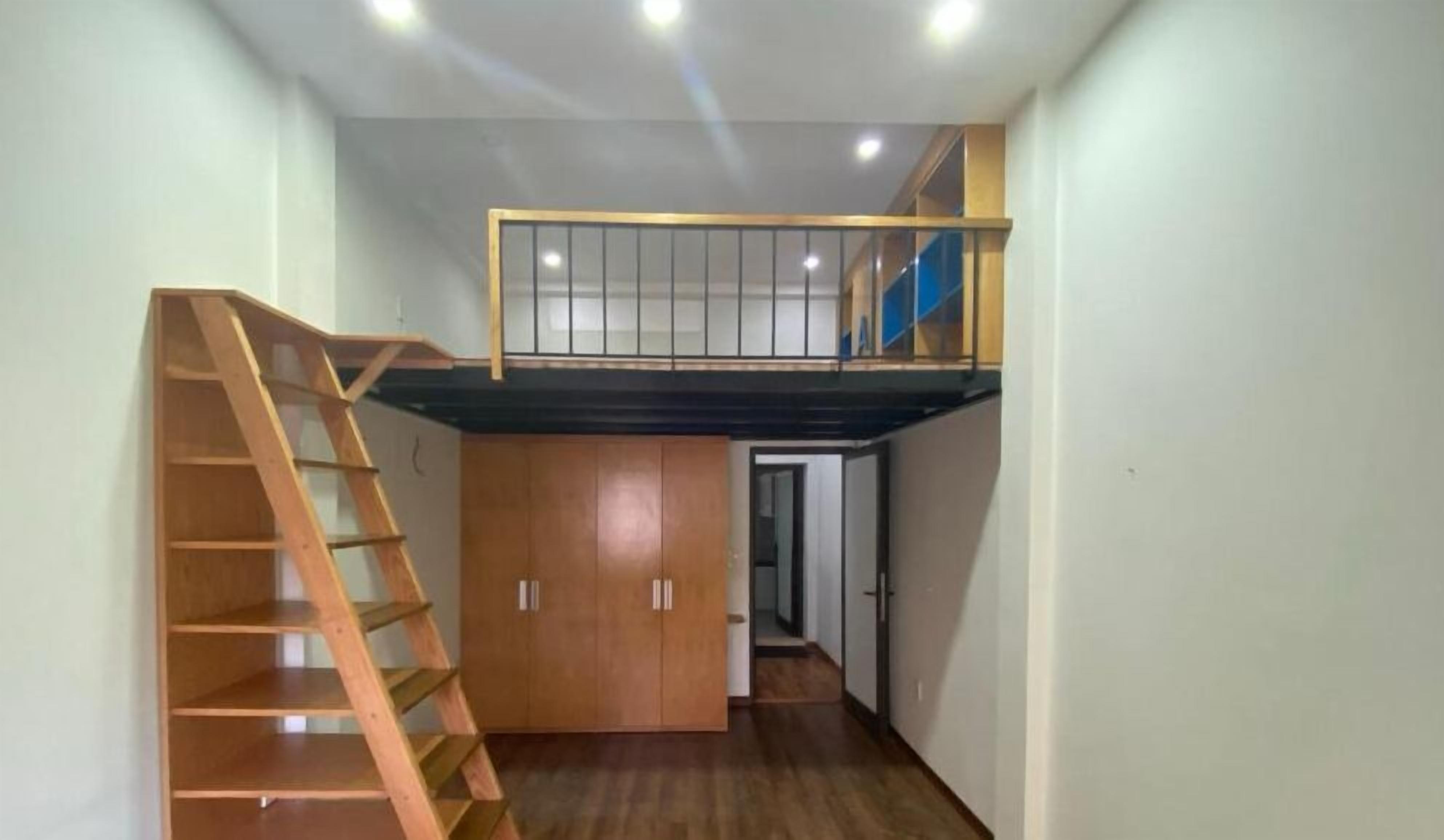 A compact room with a wooden staircase leading to a lofted area with a balcony.