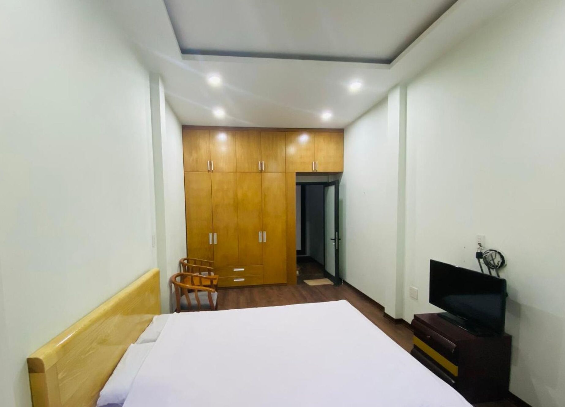 Una habitación de hotel con cama, armario de madera, una silla, televisor y escritorio.