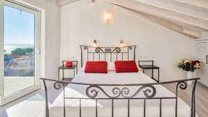 Ein Schlafzimmer mit Bett, Nachttisch, Wandleuchte und Fenster mit Blick auf Gebäude.
