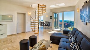 Ein modernes Wohnzimmer mit Wendeltreppe, einer schwarzen Couch und einem Essbereich mit Ausblick.