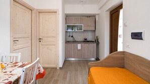 A compact room with a kitchenette, a dining area with a table and chairs, and a bed with a yellow blanket. - Agriturismo La Duchessa e il Contadino (Vieste)