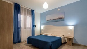 A bedroom with a bed, a nightstand, a wooden wardrobe, a window with blue curtains, and a wall-mounted light fixture. - Agriturismo La Duchessa e il Contadino (Vieste)