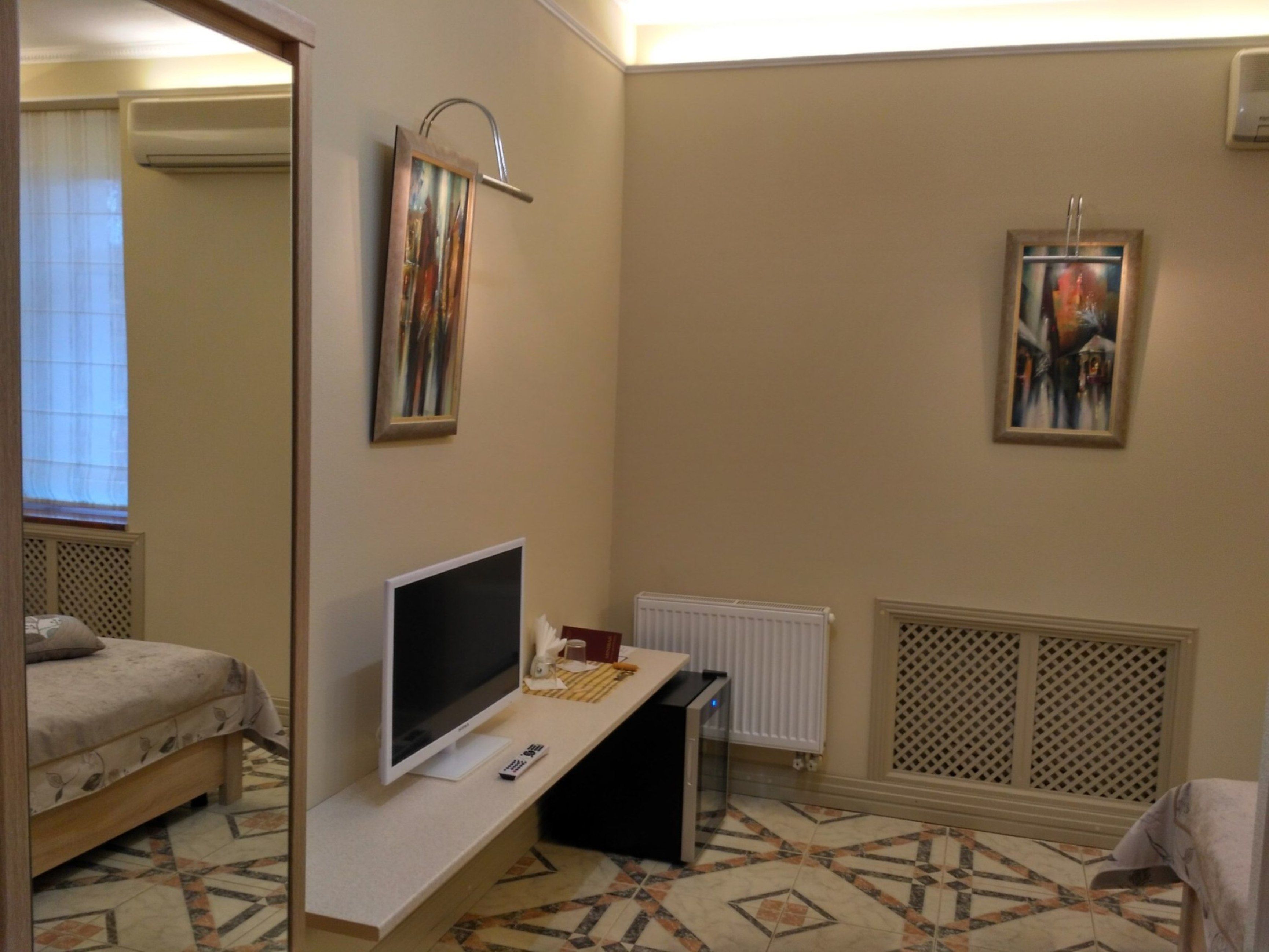 Une chambre d’hôtel avec un lit, un bureau avec une télévision, un radiateur et deux tableaux encadrés au mur.