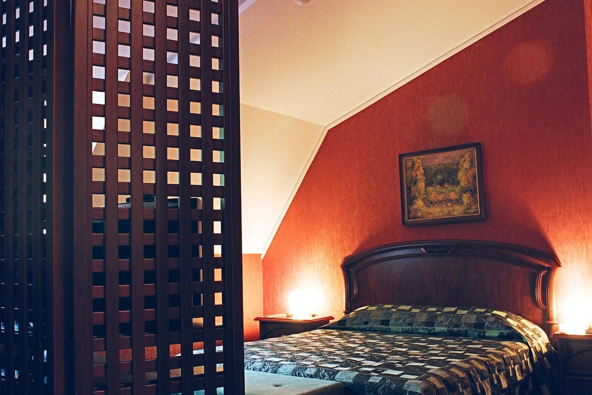 A bedroom with a bed, a wooden partition, a painting on the wall, and a patterned carpet.