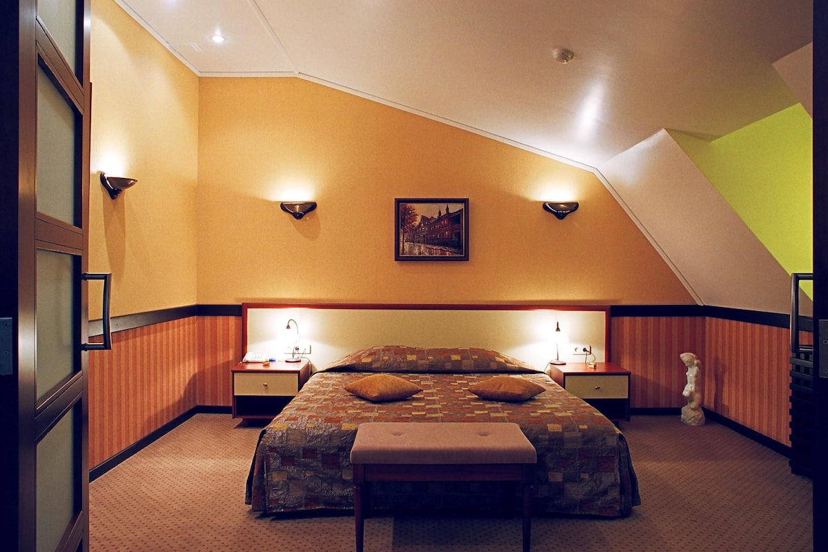 A hotel room with a large bed, two bedside tables, a nightstand, a bench, and a picture on the wall.