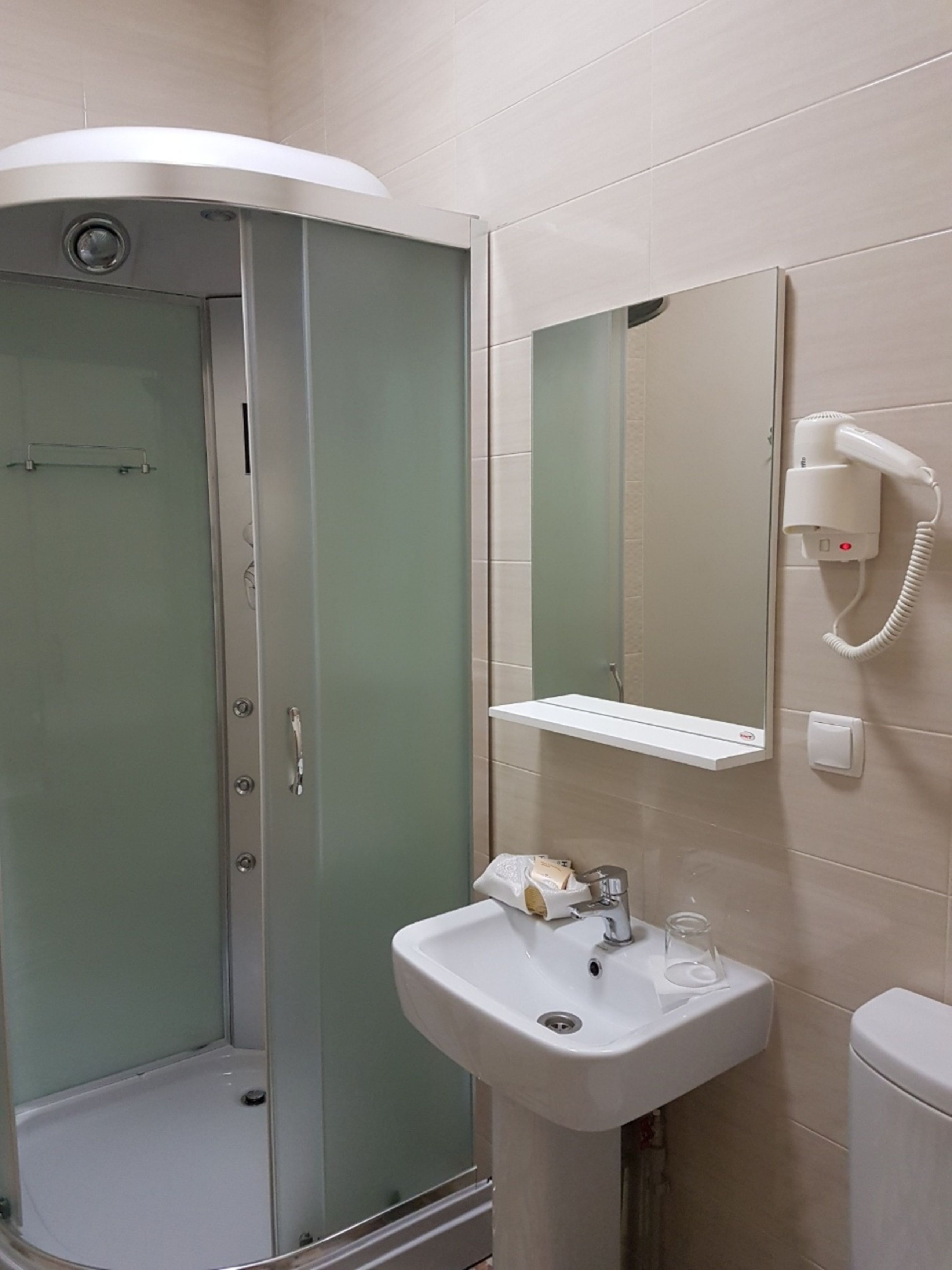 A bathroom with a glass-enclosed shower, a sink with a mirror above it, and a hairdryer on the wall.