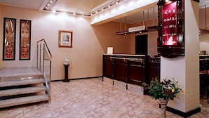 Un hall d’hôtel avec un escalier en marbre, un comptoir d’accueil, des œuvres d’art encadrées et un vase rempli de fleurs.