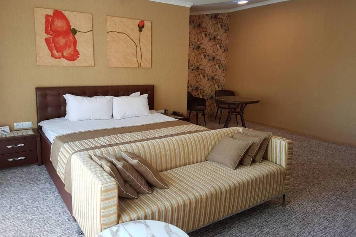 A hotel room with a large bed, a striped sofa, a small table, and two paintings on the wall.