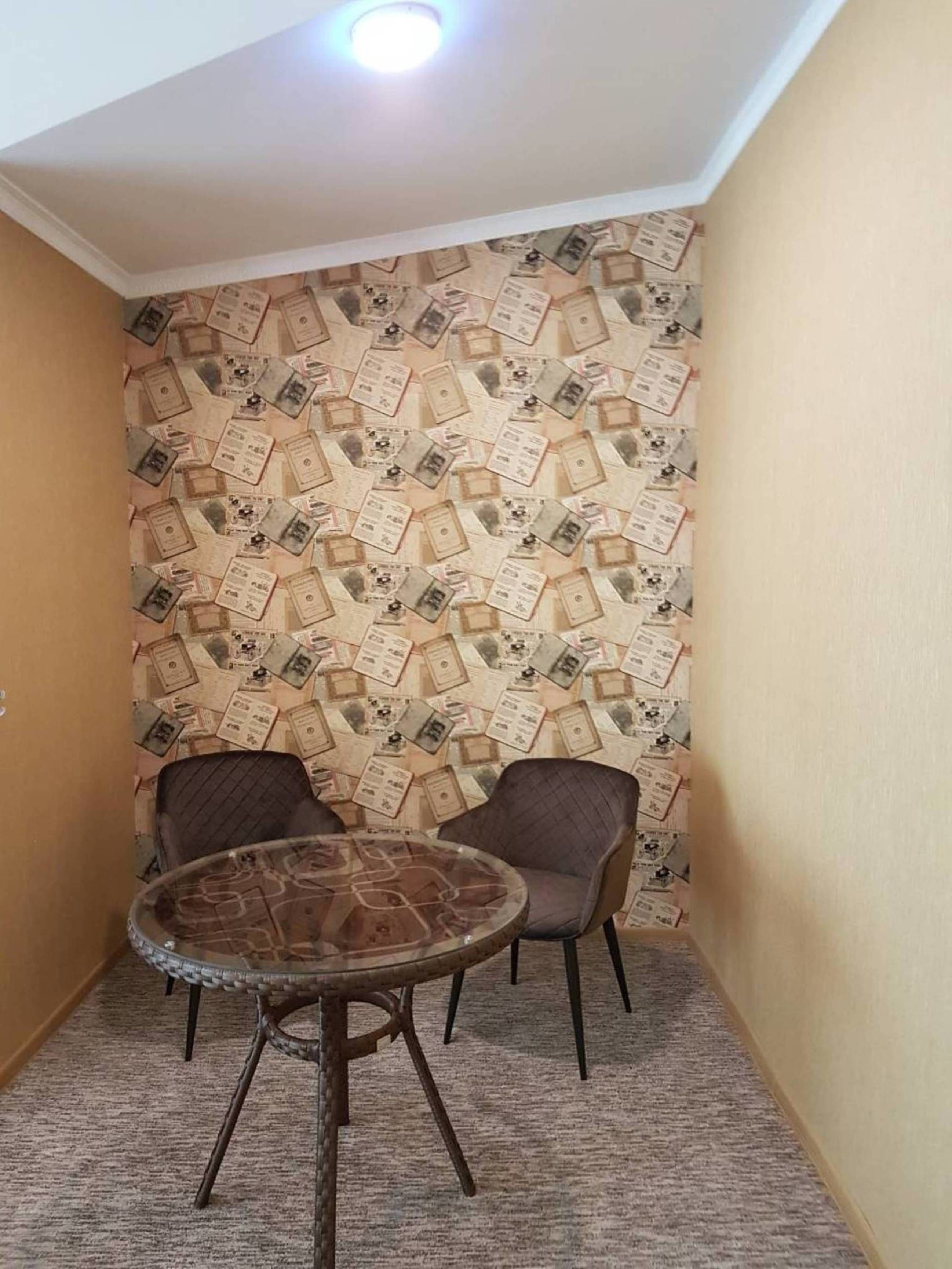 A small room with a patterned wallpaper, two chairs, and a round table.