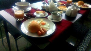 Une table de petit-déjeuner avec divers plats, notamment des œufs, des saucisses et un verre de jus d’orange.