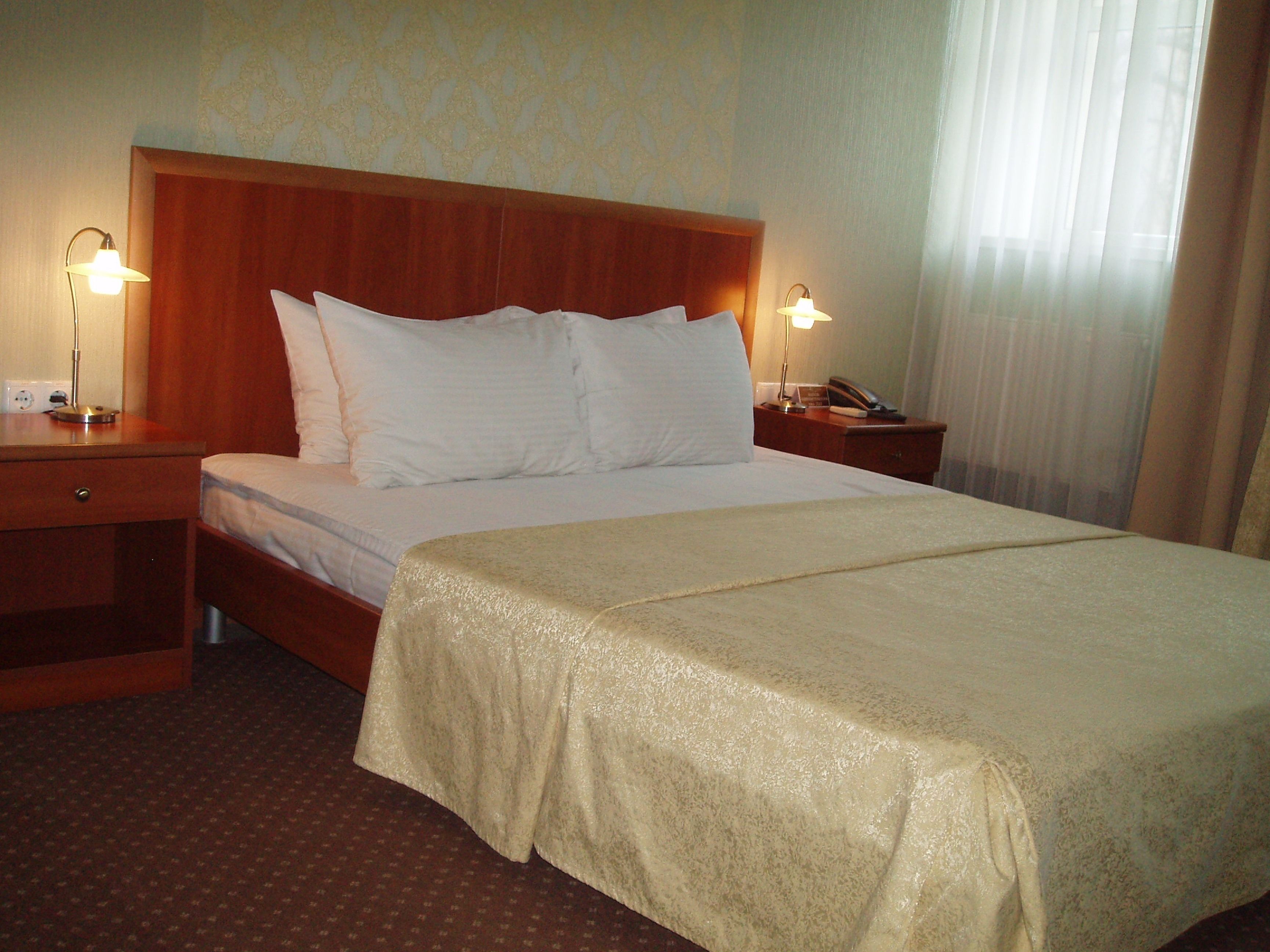 Una habitación de hotel con una cama grande, dos mesitas de noche y una mesita de noche con lámpara.