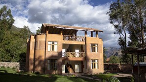 A two-story building with a balcony, surrounded by greenery and mountains. - Allin Illary Eco Hospedaje (Urubamba)