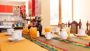 A breakfast table set with cups, a vase with flowers, and orange juice glasses. - Allin Illary Eco Hospedaje (Urubamba)