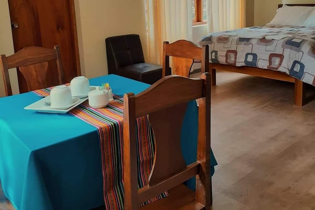 Una habitación con una cama, una mesa cubierta con mantel azul y dos sillas.