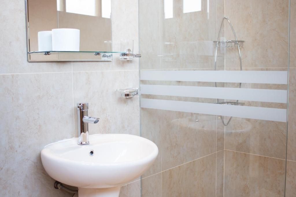 Un baño con lavamanos blanco, repisa de vidrio con artículos de aseo y zona de ducha.