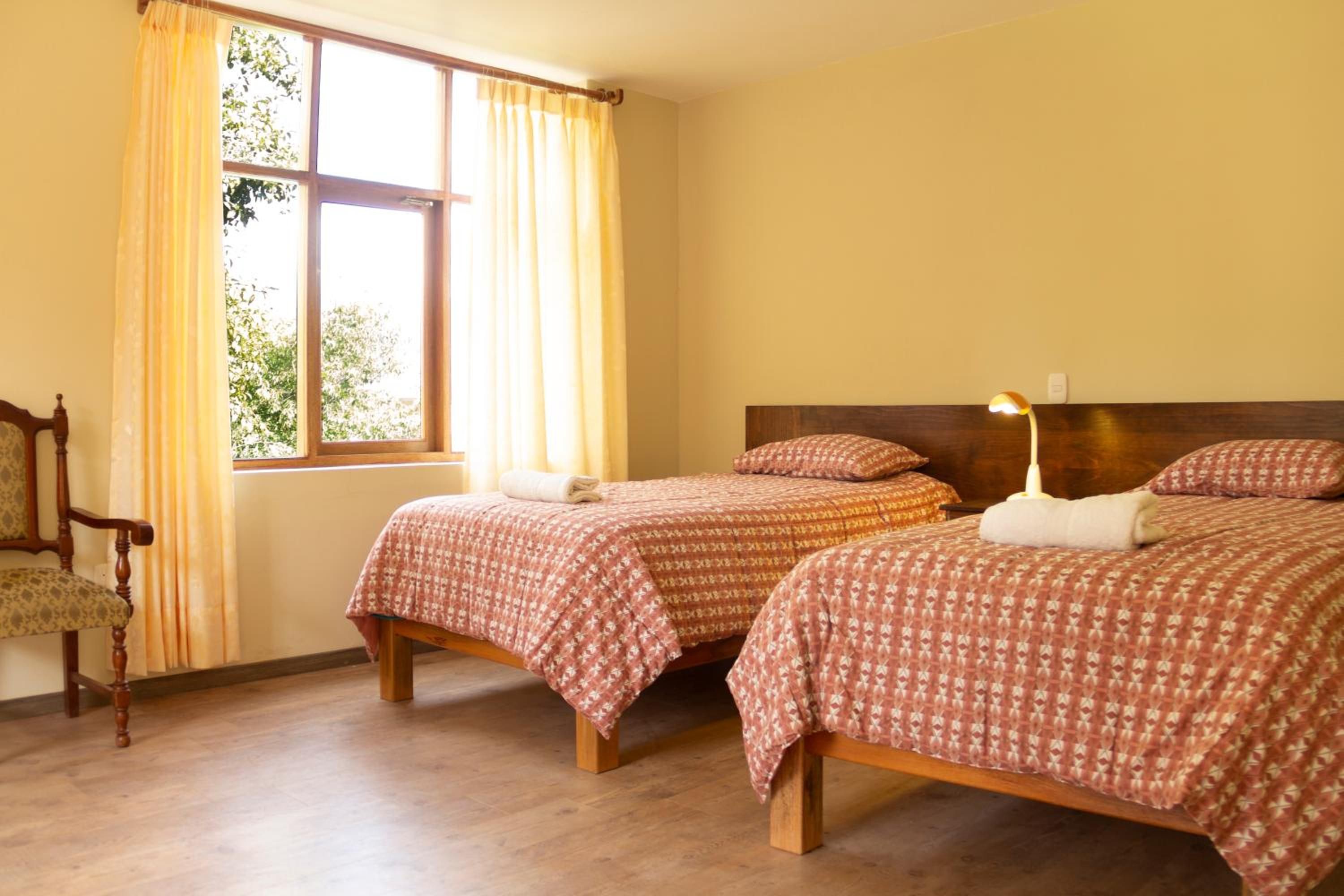 A room with two wooden beds, a chair, and a window with curtains.