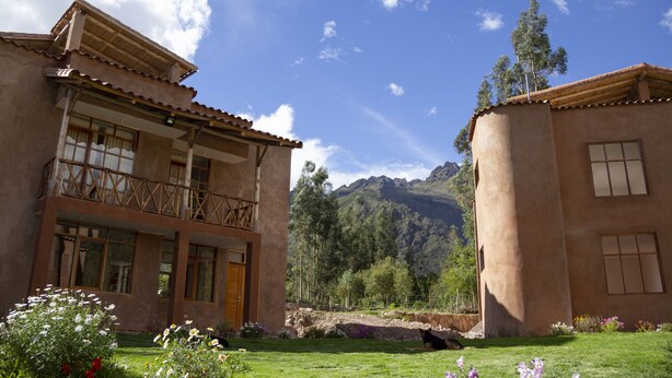 A two-story building with a balcony, surrounded by a well-maintained garden and mountains in the background. - Allin Illary Eco Hospedaje (Urubamba)