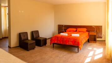 Una habitación de hotel con una cama de madera, dos sillones, una mesita y una mesita de noche.