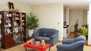 A living room with a sofa, armchairs, a coffee table, a bookshelf, and a dining area with a table and chairs. - Allin Illary Eco Hospedaje (Urubamba)