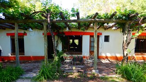 A covered patio area with a wooden pergola, outdoor seating, and a garden with various plants. - Rincón de la Finca (Luján de Cuyo)