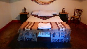 A bed with a patterned blanket, two nightstands with lamps, a chair, and a wall hanging. - Rincón de la Finca (Luján de Cuyo)
