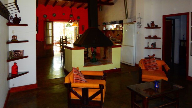 A cozy living room with a fireplace, wooden furniture, and a kitchen in the background. - Rincón de la Finca (Luján de Cuyo)