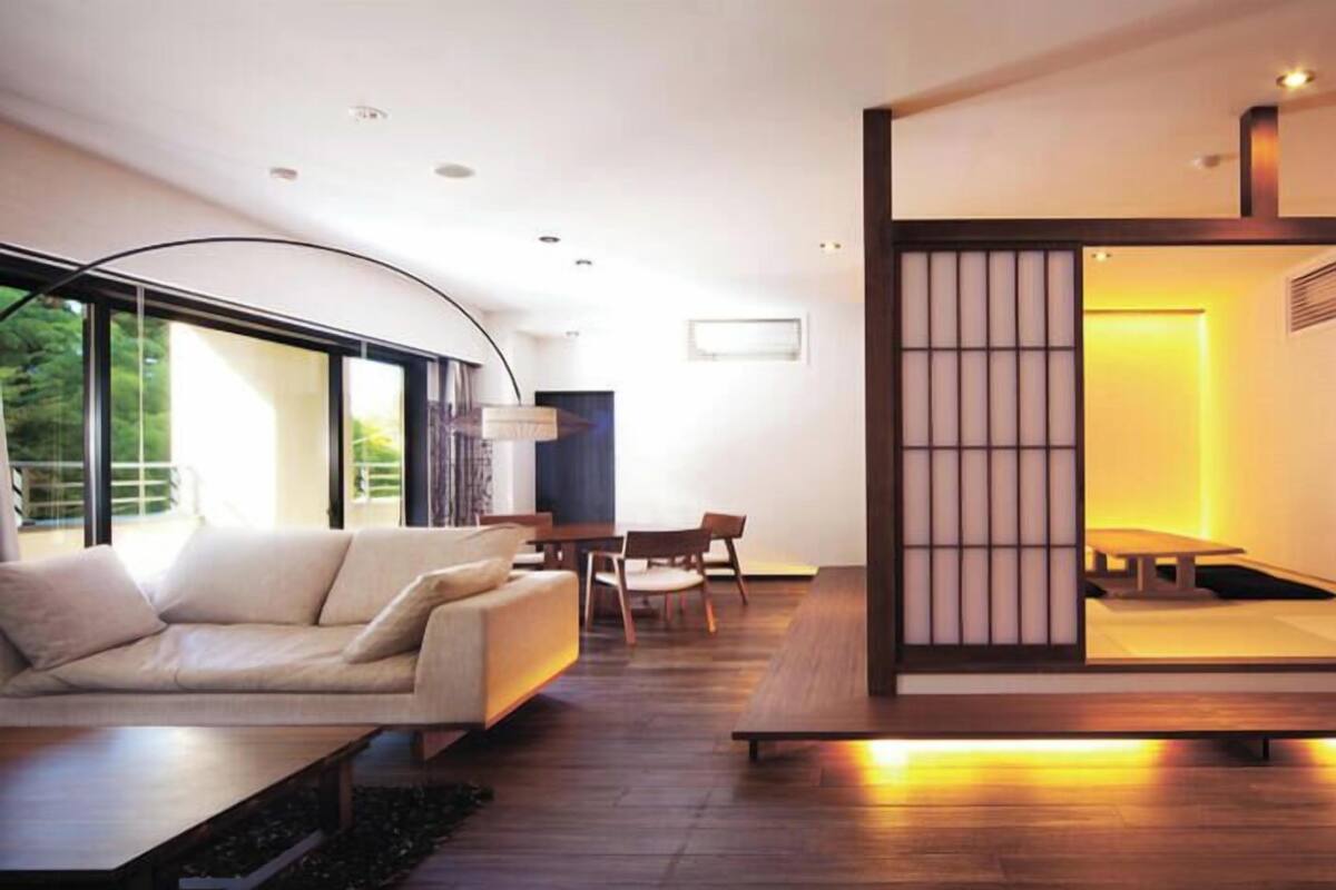 A modern living room with a sofa, dining table, and chairs, large windows, and a traditional Japanese sliding door.