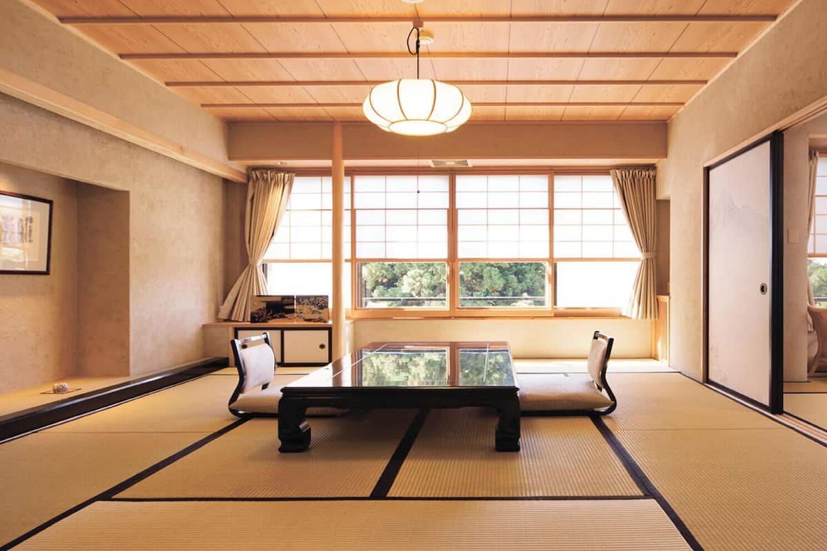 A traditional Japanese room with tatami flooring, a low table, and a hanging light fixture.