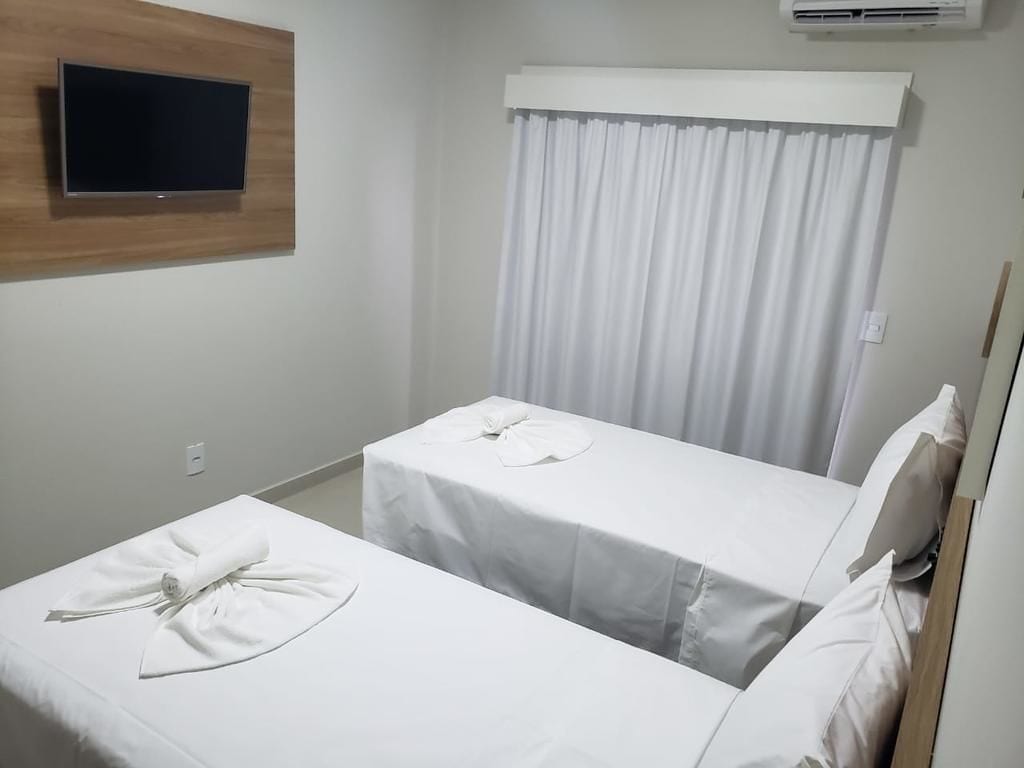 Een hotelkamer met twee eenpersoonsbedden, een flatscreen-televisie bevestigd aan een houten paneel, een wit gordijn en een witte airconditioner.