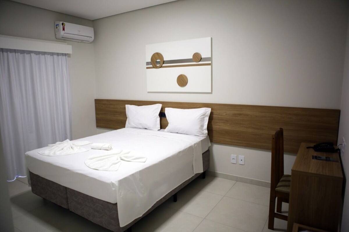 Une chambre d’hôtel comprenant un lit, une tête de lit en bois, un bureau avec une chaise et une œuvre d’art accrochée au mur.