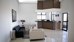 Ein großzügiger Wohnbereich mit einer schwarzen Couch, einem beigen Sessel und einem kleinen Tisch mit Blumen. Im Hintergrund ist eine Küche mit modernem Design erkennbar.